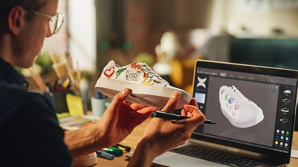 Designer looking at sneaker with 3D image in the background on computer