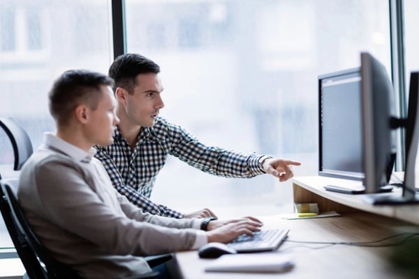 Two men working on computer with one man pointing to the screen